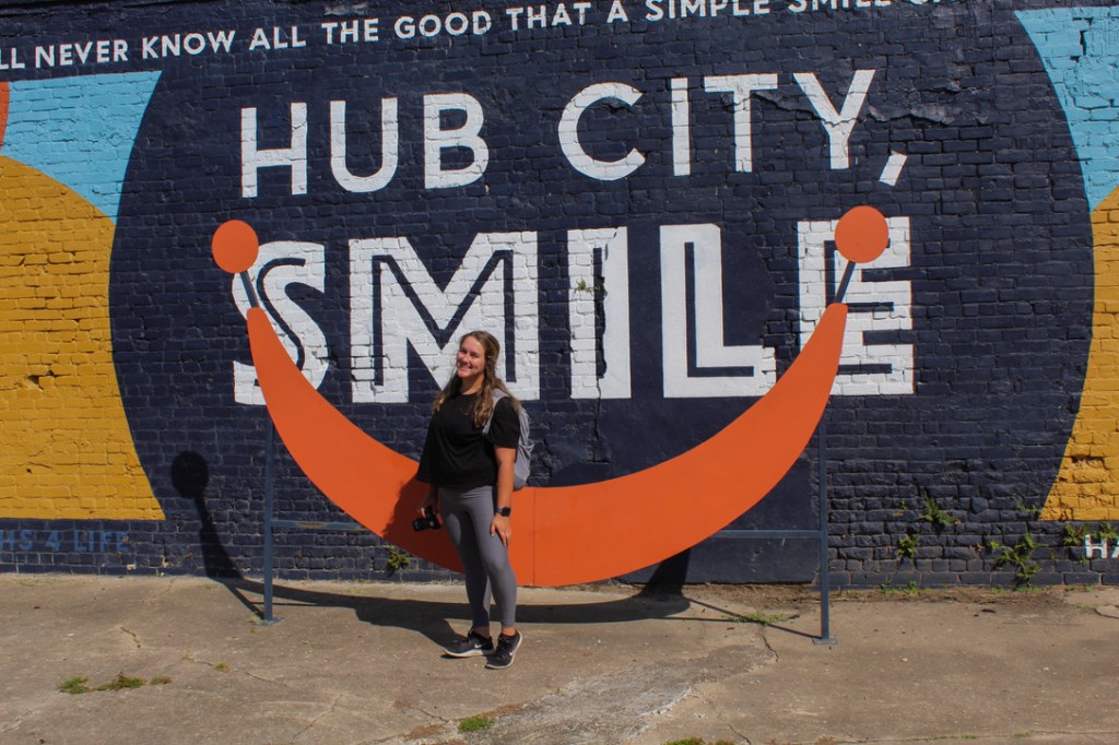 girl in front of hub city smile mural with metal smile